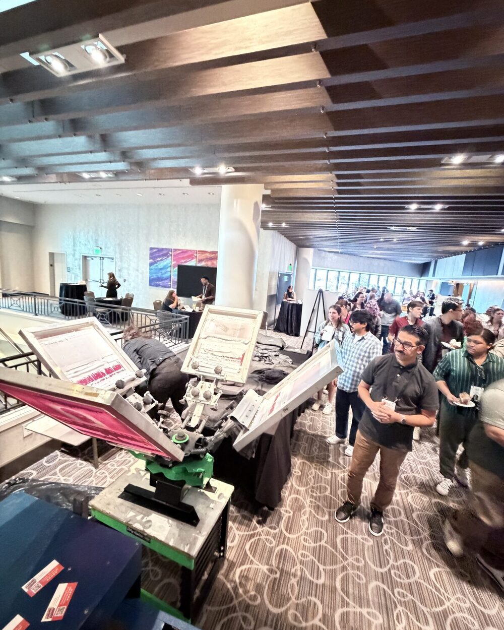 Event guests gathered around a live screen-printing press, watching shirts come off the platen