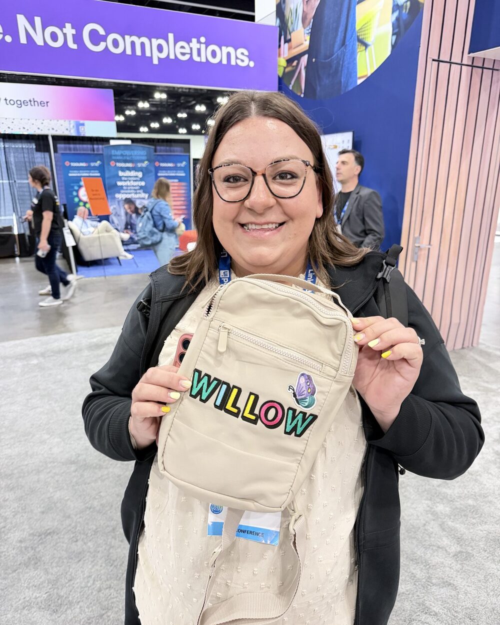 Smiling guest holding a tan crossbody bag with a name embroidered on site at a San Diego event