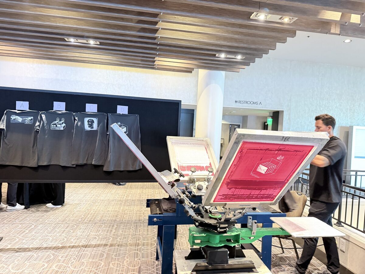 Screen-printing press set up in a bright San Diego convention-center lobby with freshly printed sample shirts on display